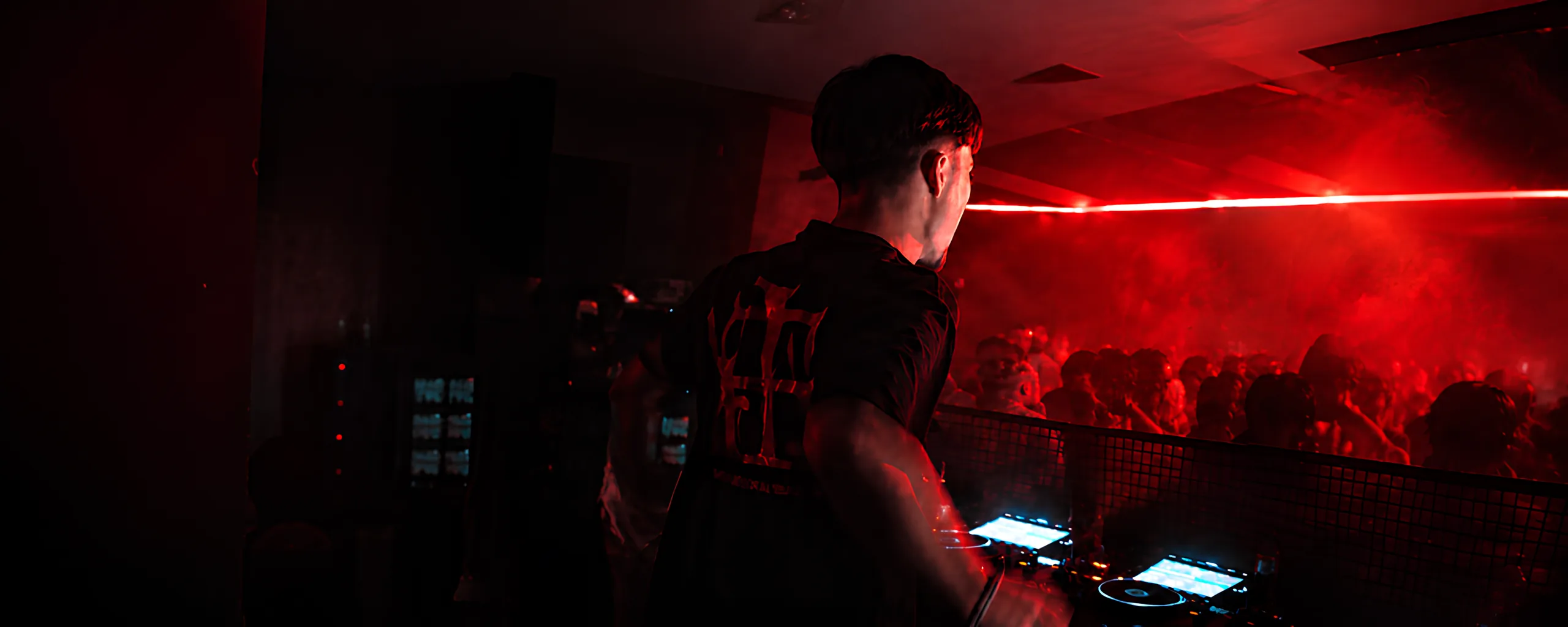 HERA behind the decks facing a crowd under deep red light